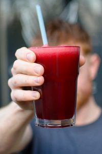 A freshly made juice at Urban Angel cafe, Edinburgh. A member of staff holds a glass up to the camera. The juice is deep red and has a straw in it.